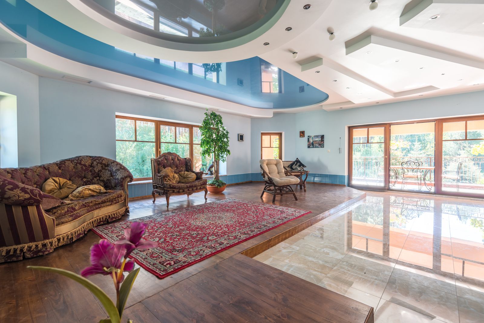 Spacious living room with a dramatic multi-level blue and white ceiling, large windows, and traditional furniture