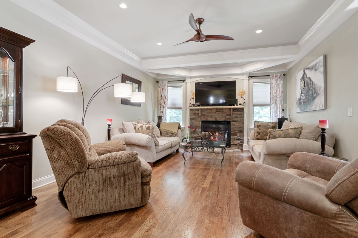 Finished family room with smooth tray ceiling, crown molding, ceiling fan, and stone fireplace