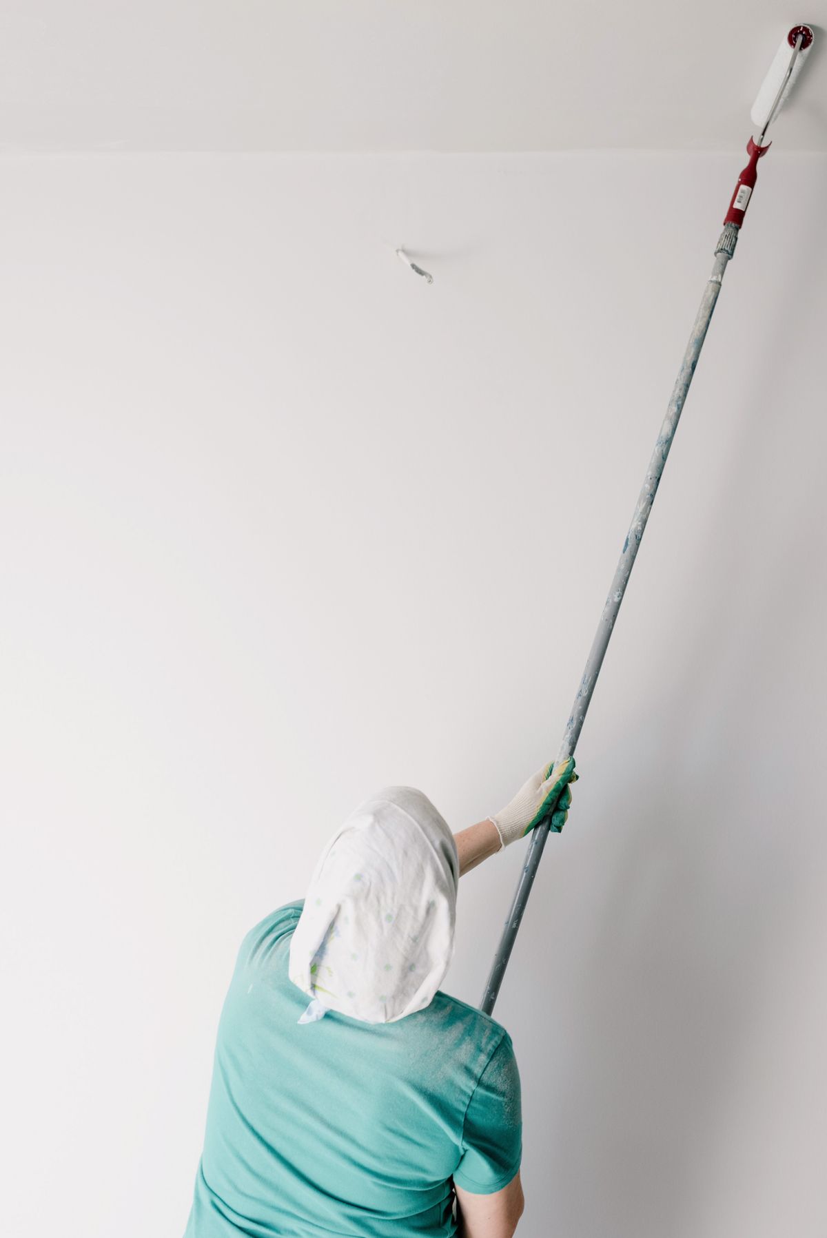 Painter in a headscarf rolling white paint onto a ceiling with an extension pole